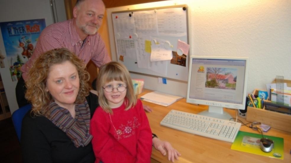 Heike van Lessen, Leiterin des Kindergartens »Bunte?Welt«, hat die Website ihres Kindergartens »auf dem?Schirm« und die vierjährige Lea Schoon auf dem Schoß. Ihr Vater Berthold, im Hintergrund, hat die Internetseite gestaltet. © Hoegen