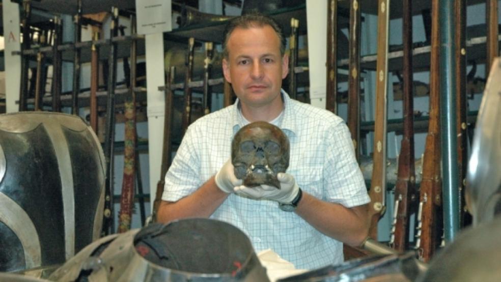 Im Magazin des Ostfriesischen Landesmuseums im Emder Stadtteil Borssum zeigt Dr. Jürgen Bär den 1930 in Nendorp gefundenen Totenschädel. Um mehr über »Joke«?zu erfahren, will der Archäologe sich bald gemeinsam mit Dr. Wolfang Jahn auch vor Ort in Nendorp sowie im Heimatmuseum Rheiderland in Weener auf Spurensuche begeben.  © Szyska