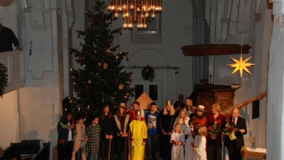 Ein musikalisches Krippenspiel führten Kinder aus Stapelmoor und Diele beim diesjährigen Noëlkonzert vor dem rot und gold geschmückten Weihnachtsbaum in der Kreuzkirche Stapelmoor auf. Waltraud Ahlers (rechts mit Blumen) leitete die 18 Mädchen und Jungen. Marianne Gerke (links) von der Kirchengemeinde Stapelmoor und Organist Stef Tuinstra (rechts) waren auch mit dabei.  © Kuper