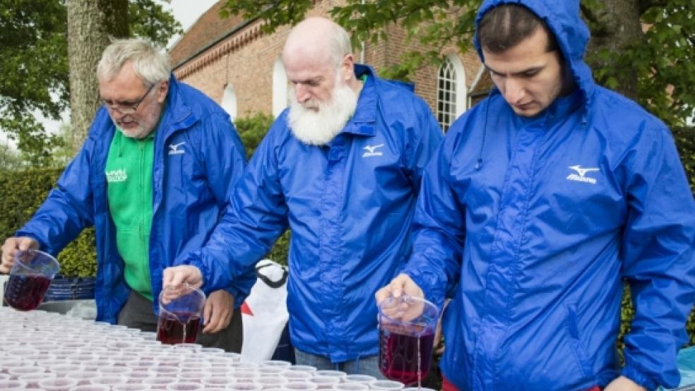 Packen an, wo sie gebraucht werden: Bruno Schachner (l.) und Burghard Borck (m.) sind beim Ossiloop im Dauereinsatz. Hier füllen sie gemeinsam mit Bilal Ortac Getränkebecher auf. © Foto: Mentrup