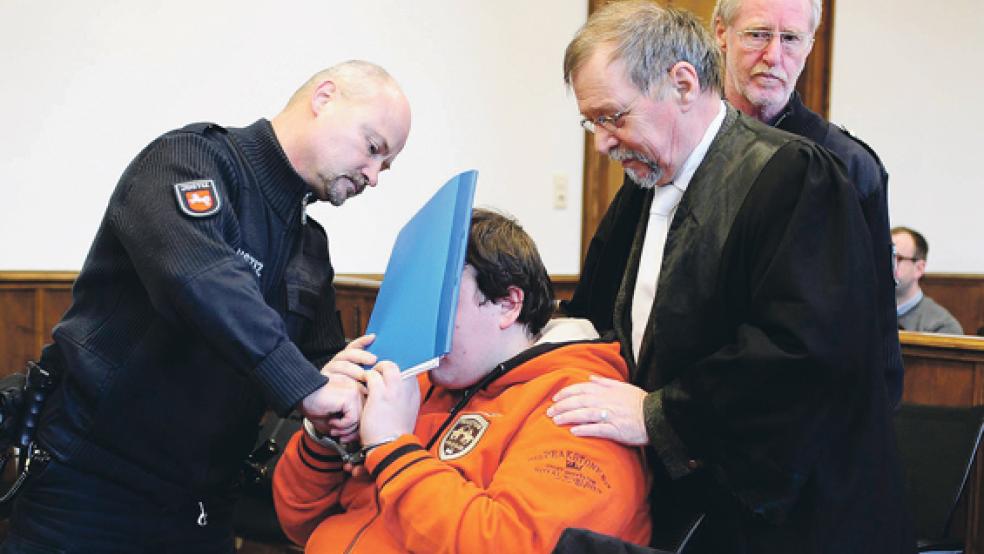 Verteidiger Klaus Rüther (Zweiter von rechts) wirkte beruhigend auf den Angeklagten ein, während seinem Mandanten die Handfesseln abgenommen wurden. Der 19-Jährige aus Brookmerland verbarg sein Gesicht gestern zum Prozessbeginn am Landgericht Aurich vor den Kameras.  © Foto: Benjamin Tebben-Willgrubs