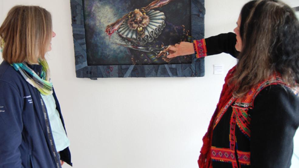 Ein düsteres Bild der ostfriesischen Künstlerin Kriso ten Doornkaat mit dem Titel »Will nichts mehr hören« schauen sich Wilma Mencke (rechts) und Agnes Ratering hier an. Mencke legt fast auf den Finger auf die Schere, mit der sich der Hase ein Stück seines Ohres abgeschnitten hat. © Foto: Hoegen