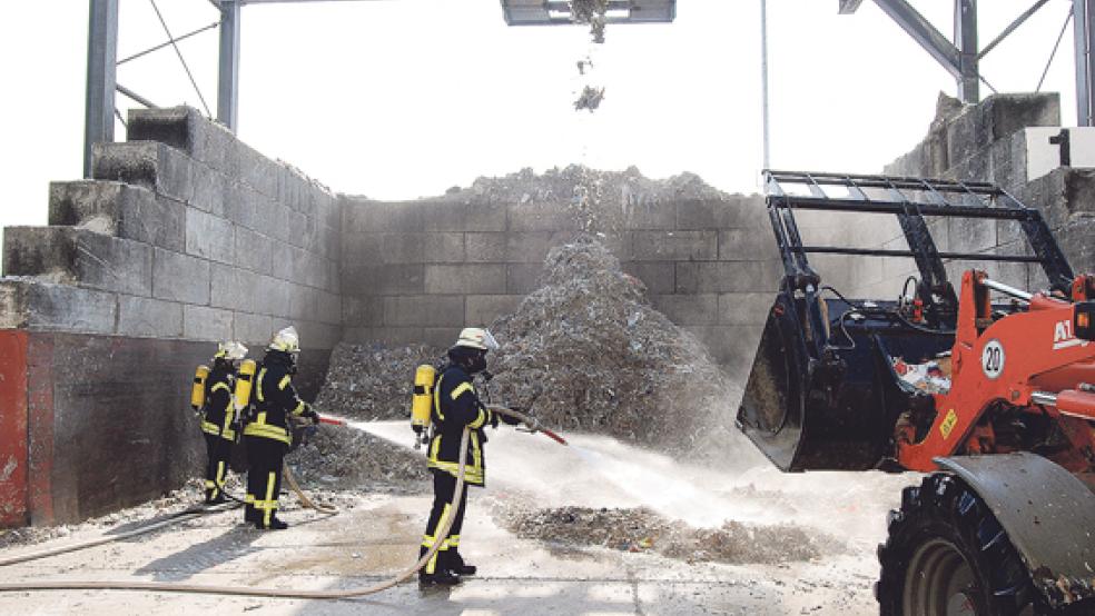 Unter schwerem Atemschutz löschen drei Feuerwehrleute die brennenden Abfälle ab. © Foto: Hoegen