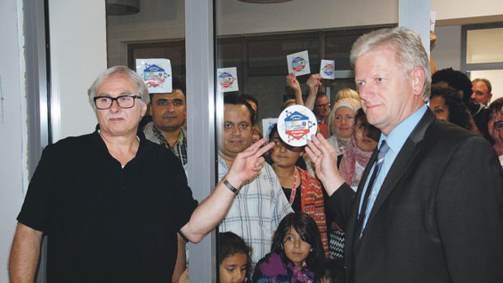 »Willkommen in Weener«: Dieter Frikke vom Arbeitskreis »Willkommenskultur Weener« (links) und Bürgermeister Ludwig Sonnenberg platzierten einen der neuen Aufkleber auf der Glaswand des Rathaus-Anbaus. © Foto: Hoegen