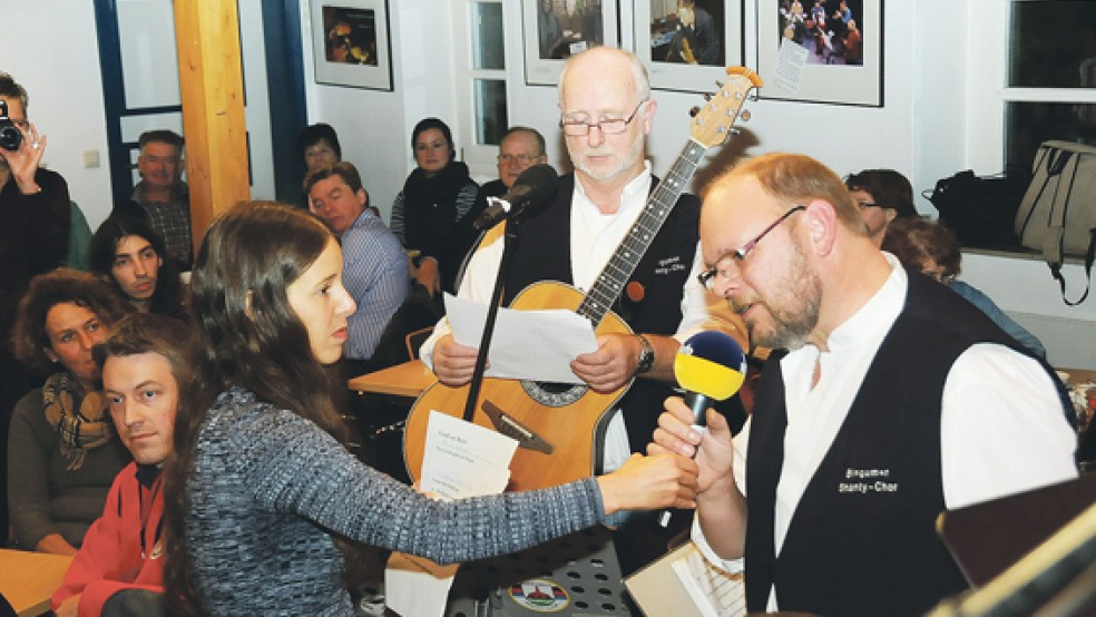 Der Vorsitzende des Bingumer Shanty-Chores, Holger Helmers (rechts), übermittelte Grüße am Mikrofon von Moderatorin Andrea Christina Furrer die Grüße an seinen Sohn, der zur See fährt und Weihnachten nicht mit seiner Familie verbringen kann. © Foto: Wolters