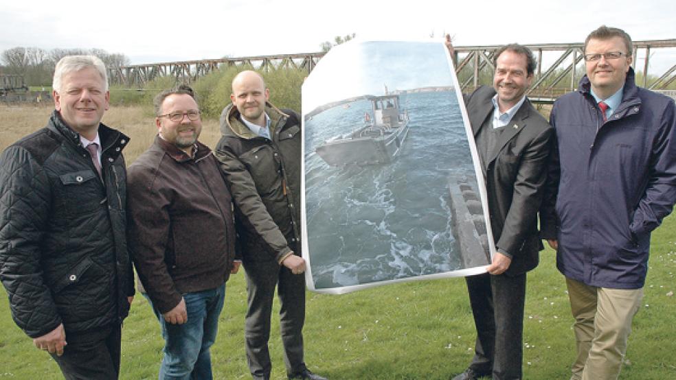 Mit einem überdimensionalen Bild der Fähre, die zwischen Weener und Westoverledingen zum Einsatz kommen soll, solange die zerstörte Friesenbrücke im Hintergrund nicht passierbar ist: Weeners Bürgermeister Ludwig Sonnenberg, der Werft-Betriebsratsvorsitzende Ludger Husmann, Werft-Geschäftsführer Tim Meyer, »Schulte & Bruns«-Chef Bengt Fischer und Westoverledingens Bürgermeister Theo Douwes (von links) gestern Nachmittag auf dem Emsdeich in Hilkenborg. © Foto: Szyska