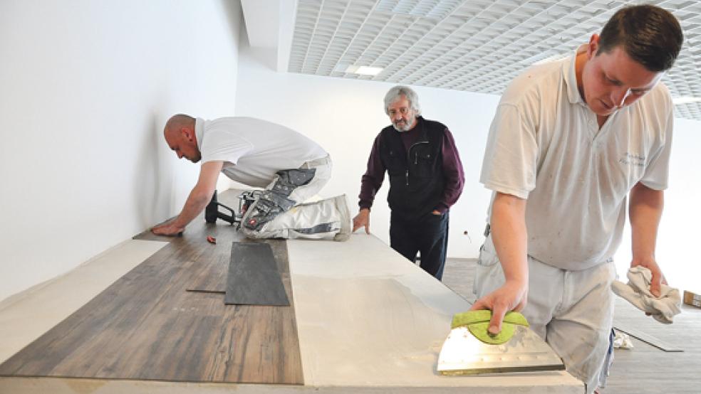 Norbert und Thomas Neumann (im Bild links und rechts) vom Malerbetrieb Siemens verlegen den neuen Boden in der Bekleidungsabteilung im Sozialen Kaufhaus an der Süderstraße in Weener. Volker Kraft (Mitte) schaut sich die Arbeiten an.  © Foto: Boelmann