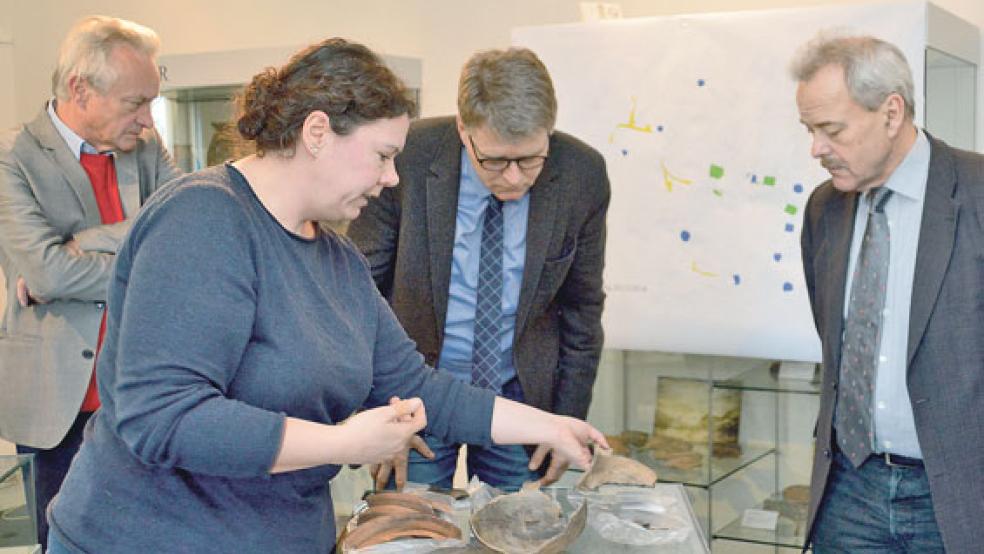Archäologin Dr. Kirsten Hüser zeigt Hesels Samtgemeindebürgermeister Uwe Themann und Hesels Gemeindebürgermeister Gerd Dählmann sowie Dr. Rolf Bärenfänger (von rechts) eine Auswahl entdeckter Fundstücke. © Foto: Former (Ostfriesische Landschaft)