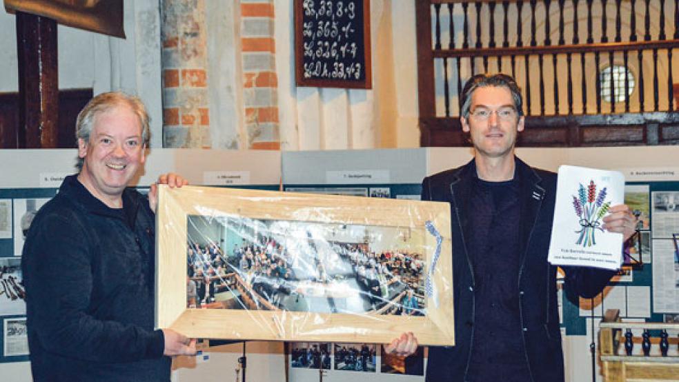 Ein Geschenk für die grenzenlose Freundschaft: Henk Bies aus Schettens (rechts) überreicht Pastor Heiko Rademaker aus Bunde ein Gruppenbild vom Besuch der Bunder im September. © Fotos: Himstedt