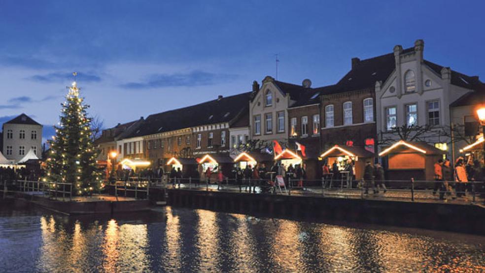 Der Adventsmarkt am Hafen in Weener begeistert viele Besucher mit den kleinen, geschmückten Holzhütten. Die Lichter spiegeln sich im Wasser und sorgen für eine besinnliche Atmosphäre vor Weihnachten. © Foto: Boelmann