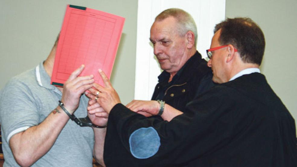 Der aus der Untersuchungshaft vorgeführte 59-jährige Angeklagte aus Emden (links) verbarg sein Gesicht, während ihm unter den Augen seines Verteidigers Folkert Adler (rechts) die Handschellen abgenommen wurden. © Foto: Ricken