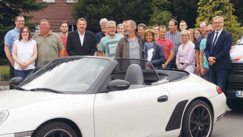 Mit einem Porsche Cabrio wurde Luitjen Kettler aus Holthusen (Bildmitte mit seiner Ehefrau Hannelore) am Donnerstag vom Wasserwerk in Weener nach Hause chauffiert. Es folgte ein Konvoi mit Verbandsfahrzeugen und den rund 20 Beschäftigten des Wasserversorgungsverbandes, die ihn auf seiner letzten Dienstfahrt begleiteten. Denn Kettler wurde nach Jahrzehnte langer Tätigkeit als Wasserwerkswärter in den Ruhestand verabschiedet. © Foto: WVV
