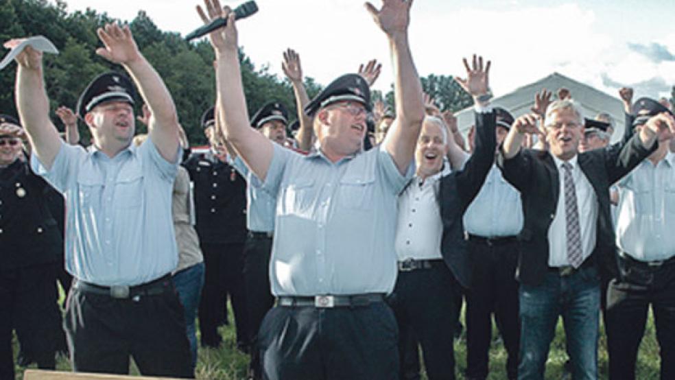Hoch die Hände: Nicht nur die Funktionsträger der Kreisfeuerwehr um Organisationsleiter Timo Smit (Zweiter von links) machten mit - auch Landrat Matthias Groote und Weeners Bürgermeister Ludwig Sonnenberg streckten sich, als die »La Ola«-Welle am Mittwochabend über den Platz schwappte. © Szyska