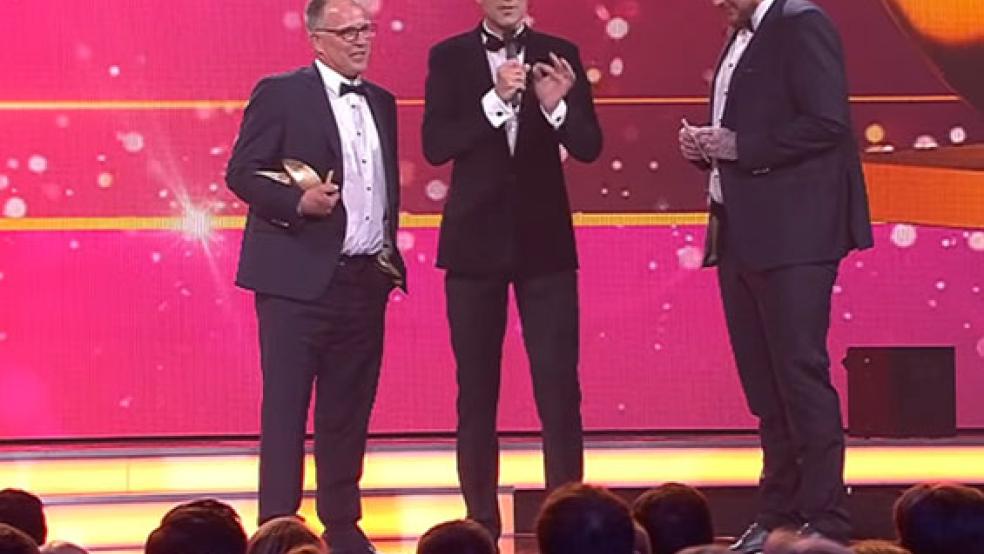 Raus aus dem Anzug, rein ins Trikot: Torwart Wilke Zierden spielt seit 16 Uhr mit dem SuS Steenfelde gegen den SV Wymeer-Boen. Im Bild links SuS-Platzwart Udo Tesch, in der Mitte Moderator Kai Pflaume. © Screenshot: RZ