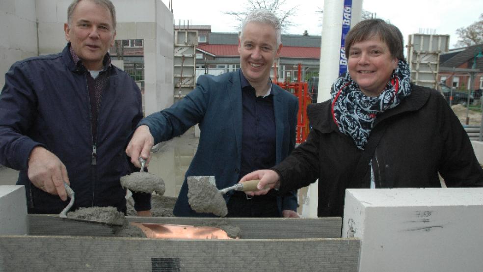 Mauerten ein Kupferrohr als »Zeitkapsel« mit einer aktuellen »Rheiderland Zeitung«, Bauplänen und Geldmünzen in eine Wand des Familienzentrums ein: Bundes Bürgermeister Gerald Sap, der Leeraner Landrat Matthias Groote und die Oldenburger Architektin Christine Müller (von links). © Foto: Szyska