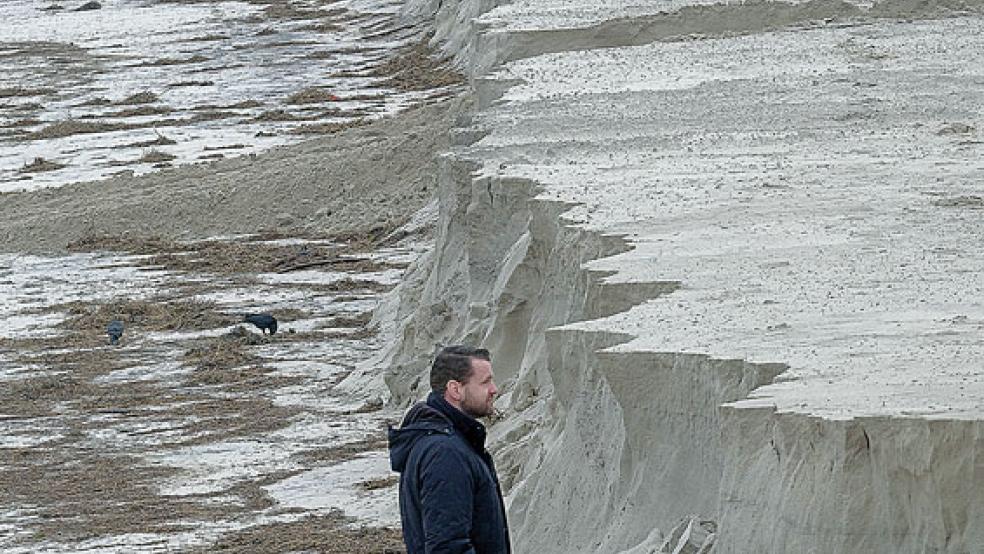 Wangerooges Bürgermeister Marcel Fangohr spaziert an der Abbruchkante des Strandes entlang. Die Sturmfluten der letzten Woche haben vor allem den Inseln zugesetzt. © Foto: Stollarz/dpa