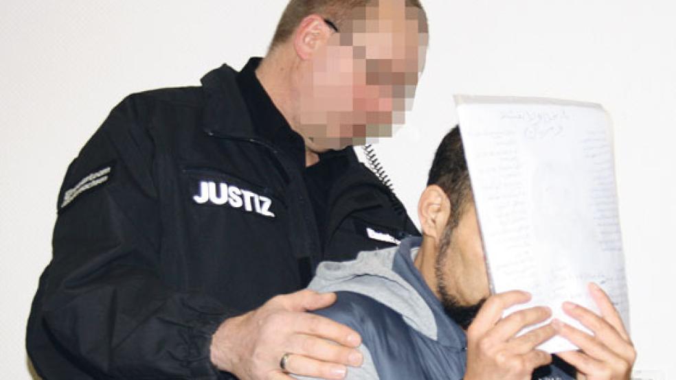 Ein Justizwachtmeister führte den Angeklagten, der sein Gesicht verbarg, gestern beim Prozessauftakt im Landgericht in Aurich sicher zu seinem Sitzplatz. © Foto: Ricken