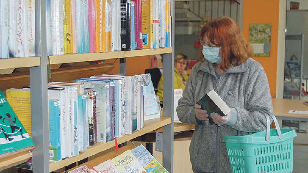 Ein noch ungewohntes Bild: Eine Besucherin der Stadtbücherei Weener mit Alltagsmaske stöbert im Bücherregal. Im Hintergrund Bücherei-Mitarbeiterin Birgitt de Riese. © Foto: Hoegen