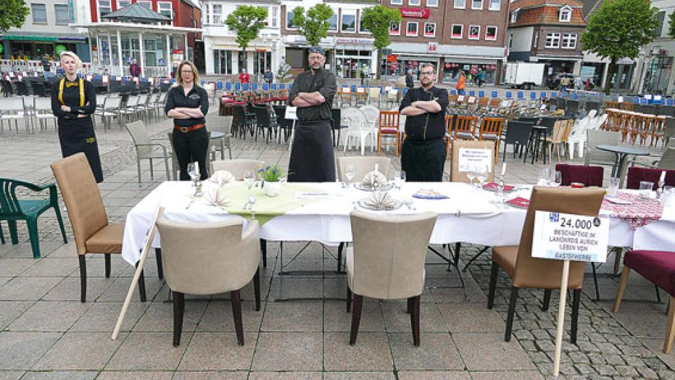»Stiller Protest« mit Tischen und Stühlen auf dem Marktplatz in Aurich (von links): Alina Krüger (»Hotel am Schloss«), Mareike Zägel (Hotel »Stadt Aurich«) und Peter Lachnicht (»Hochzeitshaus«) sowie Dirk Bach (»Hafen Extra«). © Foto: Jürgens