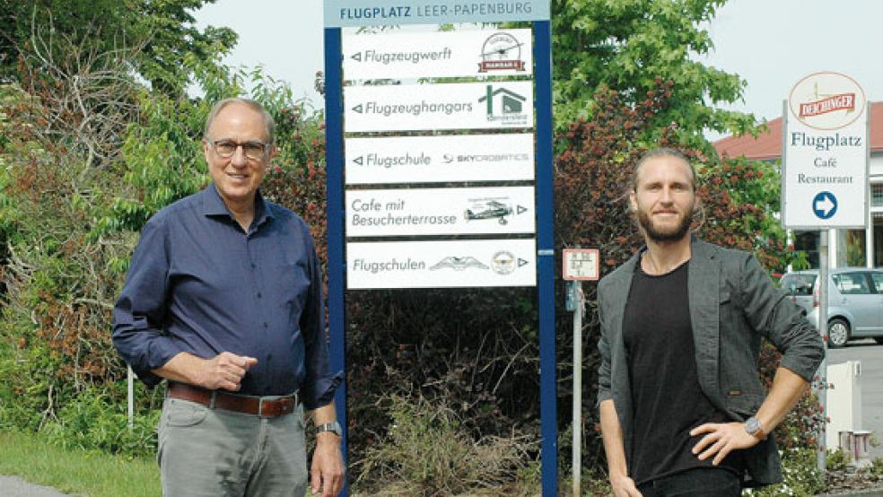 Flugplatz-Geschäftsführer Dieter Backer (links) freut sich über die Ansiedlung der Flugwerft von Adrian Schmer (rechts). Das neue Hinweisschild dokumentiert, wie breit der Flugplatz im Jubiläumsjahr aufgestellt ist. © Foto: Szyska