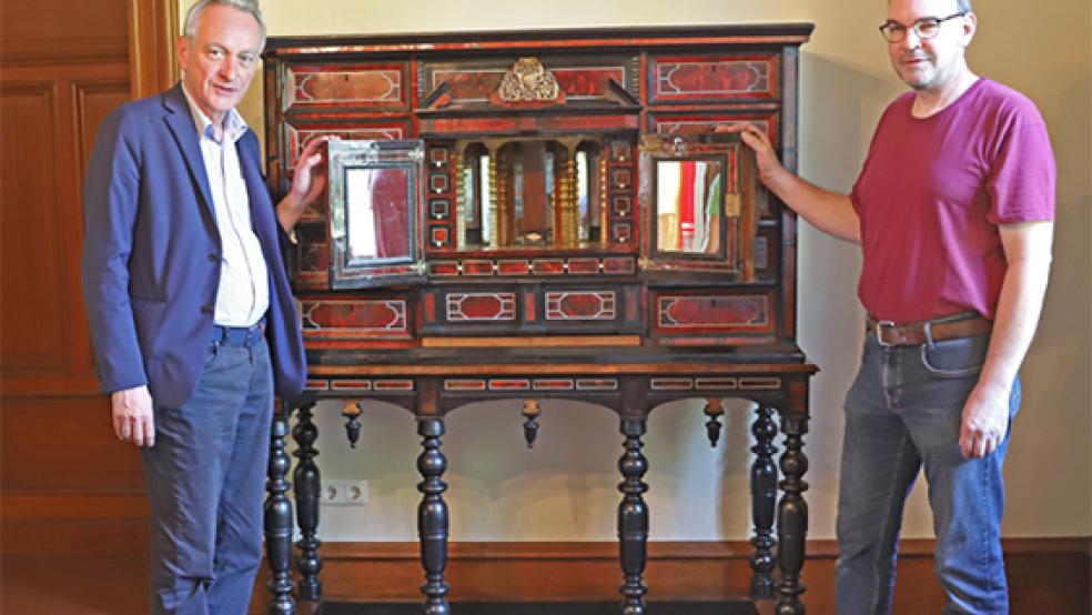 Der Kabinettschrank stand früher vielleicht im Haus Cirksena. Jetzt ist er restauriert zur Ostfriesischen Landschaft zurückgekehrt. Dr. Rolf Bärenfänger, Direktor der Ostfriesischen Landschaft, und Restaurator Reiner Peppelenbosch präsentieren das Möbelstück. © Foto: Reese/Ostfriesische Landschaft