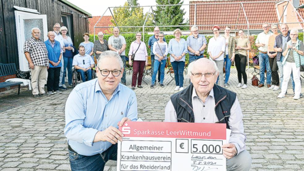 Klinikum Leer-Geschäftsführer Holger Glienke überreicht dem Vorsitzenden des Allgemeinen Krankenhausvereins, Jakobus Baumann, eine Spende für den ehrenamtlichen Einsatz von Helfern im Testzentrum – im Hintergrund Helfer mit Angehörigen und Beteiligte des Testzentrums am Krankenhaus Rheiderland. Hinweis: Alle beteiligten Personen sind entweder doppelt geimpft oder getestet gewesen.  © Foto: privat