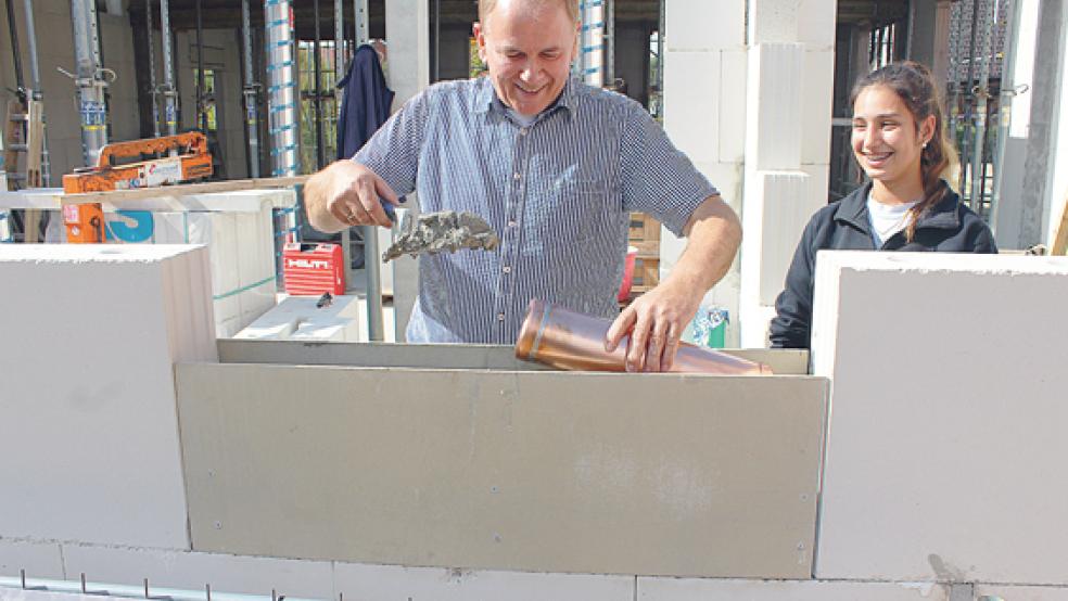 Unter dem prüfenden Blick der Maurer-Auszubildenden Sabina Zegrek mauert Bürgermeister Gerald Sap beim Kindergarten in der Birkenstraße in Bunde die »Zeitkapsel« in den Grundstein des Gebäudes ein.  © Foto: Berents