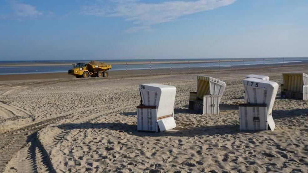 Ein Muldenkipper, ein sogenannter Dumper, beladen mit Sand aus einem Reservoir im Inselosten fährt an Strandkörben vorbei am Strand der Insel Baltrum. Winterstürme hatten große Teile des Badestrandes fortgespült - daher beginnen nun auf der kleinsten ostfriesischen Insel Baltrum die Sandaufschüttungen. © Dembski (dpa)
