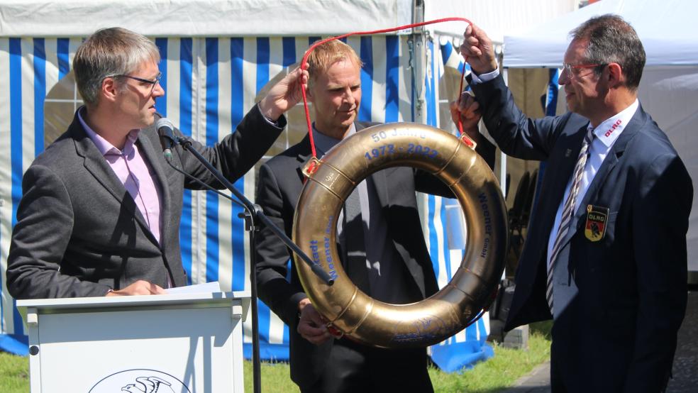 Bürgermeister Heiko Abbas und Friesenbad-Geschäftsführer Hermann Welp überreichen dem 1. Vorsitzenden der DLRG, Norbert Loger, zum Jubiläum einen goldenen Rettungsring. © Busemann