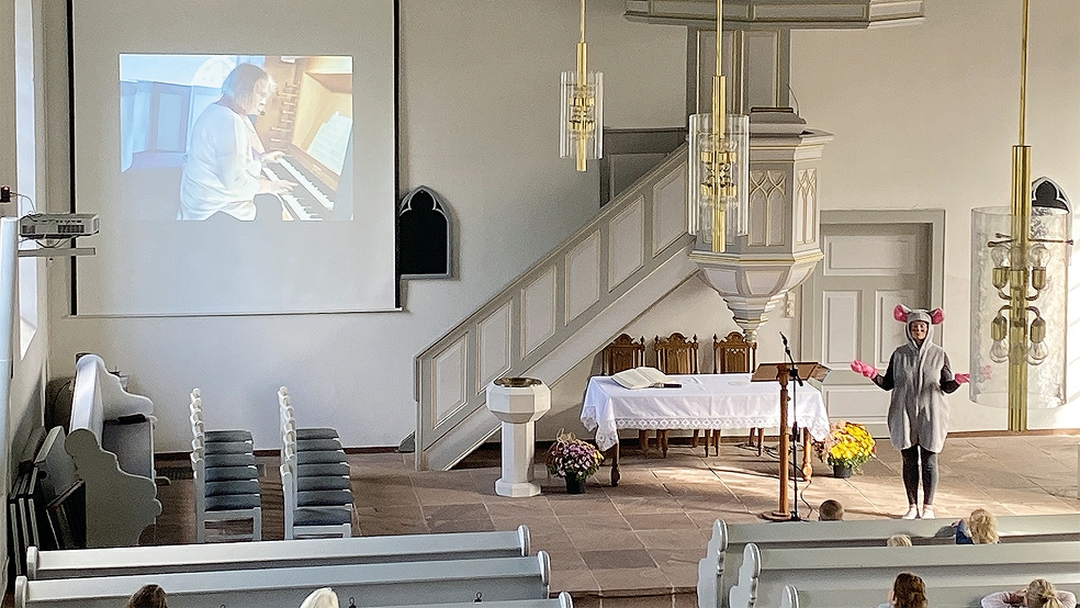 Kirchenmaus »Charly« stellte Fragen und Organistin Gertrud Velte (auf der Leinwand) erklärte in Holthusen die Führer-Orgel in der reformierten Kirche.  © Foto: Kuper