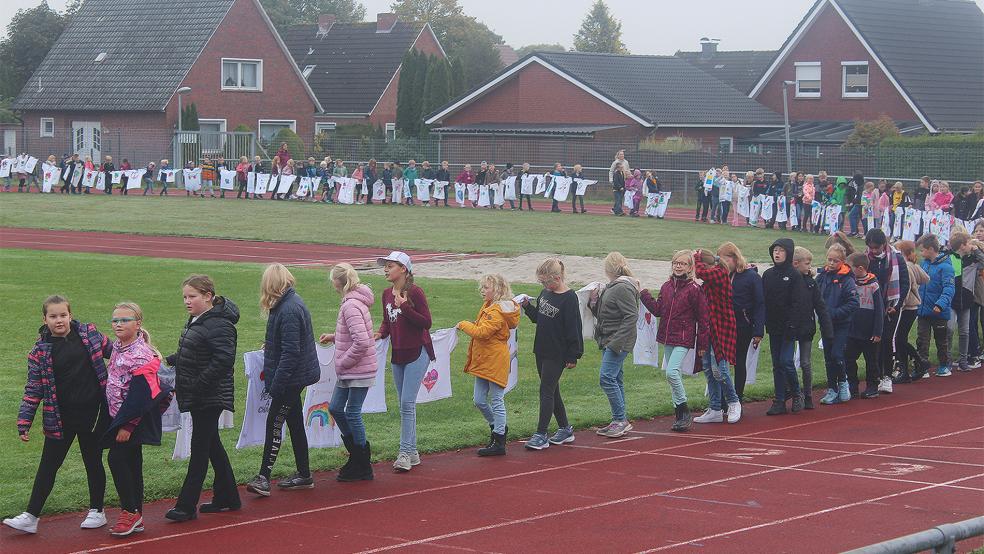 Die Bunder Grundschüler marschierten mit einer Friedensleine aus selbst verzierten T-Shirts um die Laufbahn des Sportplatzes am Mölenland.  © Foto: Berents