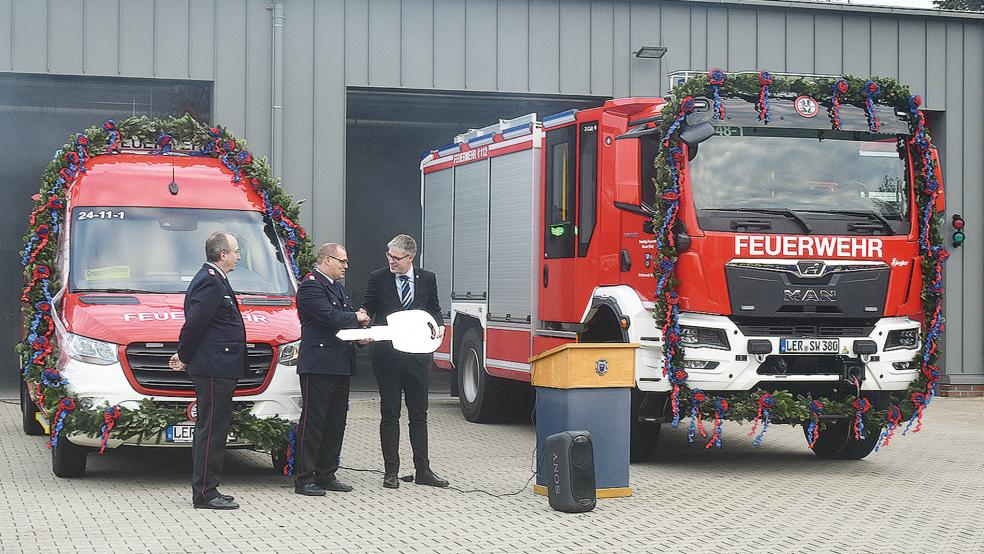 Mit einem überdimensionalen Schlüssel als Symbol überreichte Bürgermeister Heiko Abbas (rechts) zwei neue, mit Girlanden geschmückte Einsatzfahrzeuge an Stadtbrandmeister Jörg Fisser (Mitte) und Ortsbrandmeister Hans-Joachim Kotulla. Links der Einsatzleitwagen (ELW), der bereits seit 2020 benutzt wird, rechts das neue Hilfeleistungslöschgruppenfahrzeug (HLF 20).  © Kuper