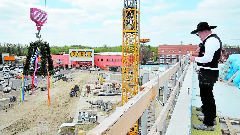 Während der 20-jährige Zimmermann Jannes Gödiker vom Bauunternehmen Schulte aus Haselünne auf dem Dach des Ems-Center-Rohbaus den Richtspruch vorlas, wurde mithilfe eines Krans der Richtkranz emporgehoben.  © Schade