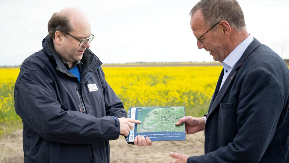 Der Emder Obersielrichter Reinhard Behrends (rechts) übergibt Niedersachsens Umweltminister Christian Meyer (Grüne) an einer Deichbaustelle eine Ergebnisbroschüre des Forschungsprojektes »Klever-Risk«.  © Schuldt (dpa)
