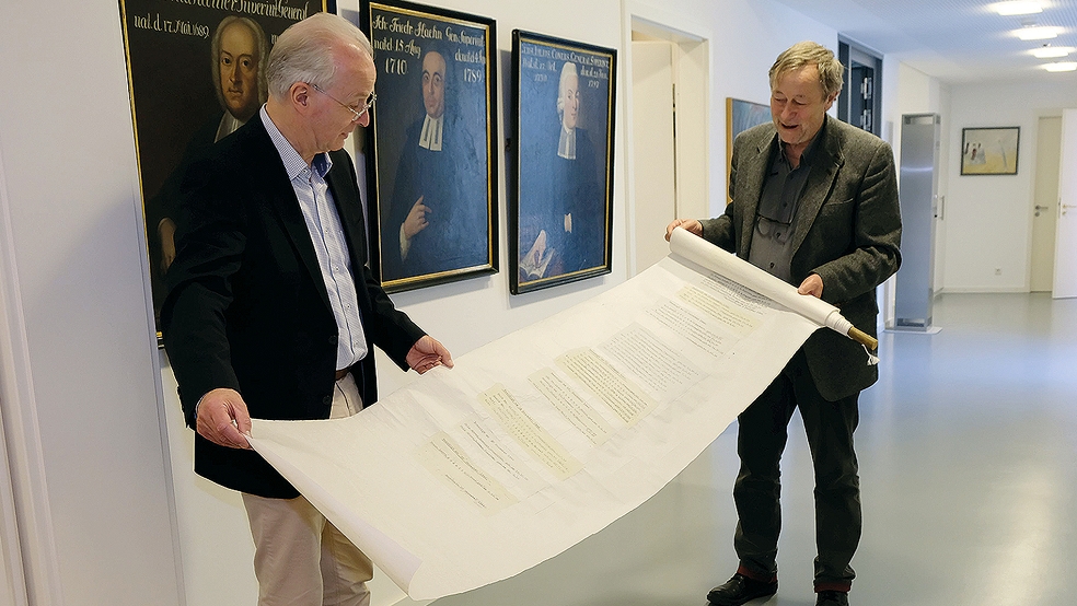 Künstler Herbert Müller (rechts) zeigt Dr. Detlef Klahr die Installation »Totenzettel« mit den 188 Namen der KZ-Opfer aus Engerhafe auf acht Meter langem Japanpapier.  ©  Foto: Grundmann