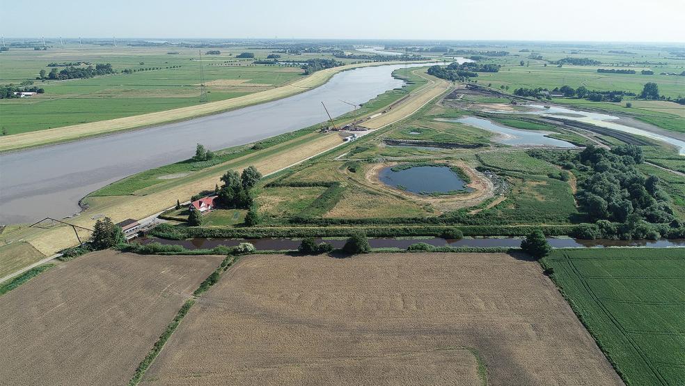 Blick auf den künftigen Tidepolder: Links der Ems ist das Rheiderland zu sehen. Am rechten Ufer ist zu erkennen, dass der Deich zum Fluss hin geöffnet wurde. Dort entsteht das Einlassbauwerk, das den Flut- und Ebbstrom auf die Fläche regeln soll. Vorn in der Mitte ist ein Süßwasserteich, dahinter ist das Sedimentationsbecken, rechts oben liegen Priele.  © Foto: Bauunternehmen Ludwig Freytag