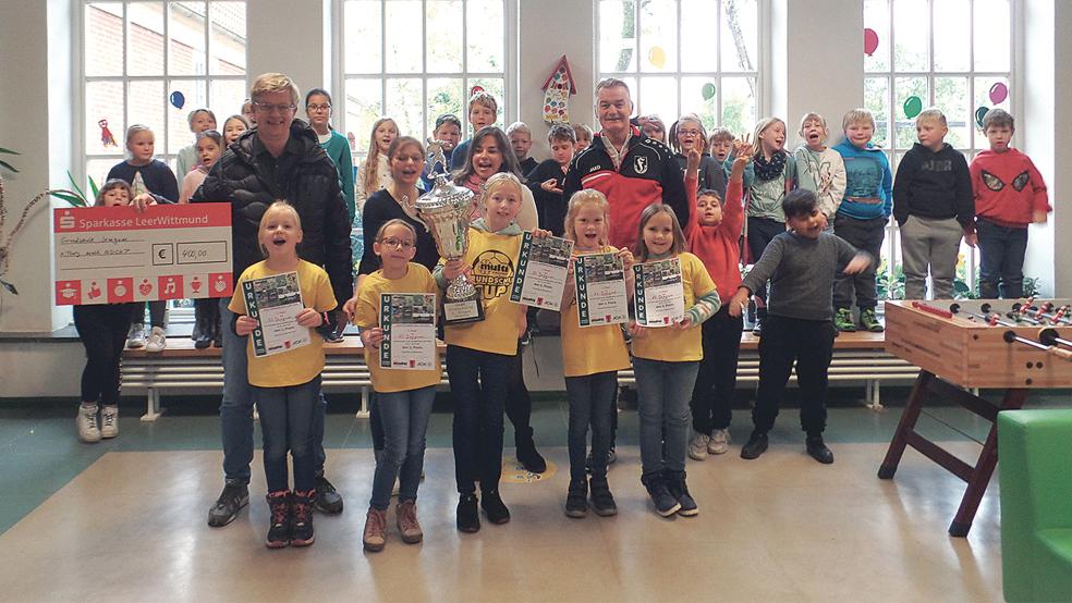 Matthias Brahms (Multi Süd), Cassandra Veenker (Lehrerin), Elisa Hahn (Lehrerin) und Reiner Voskamp (Frisia Loga) sowie die siegreichen Schülerinnen bei der Scheckübergabe an der Grundschule in Jemgum.  © 