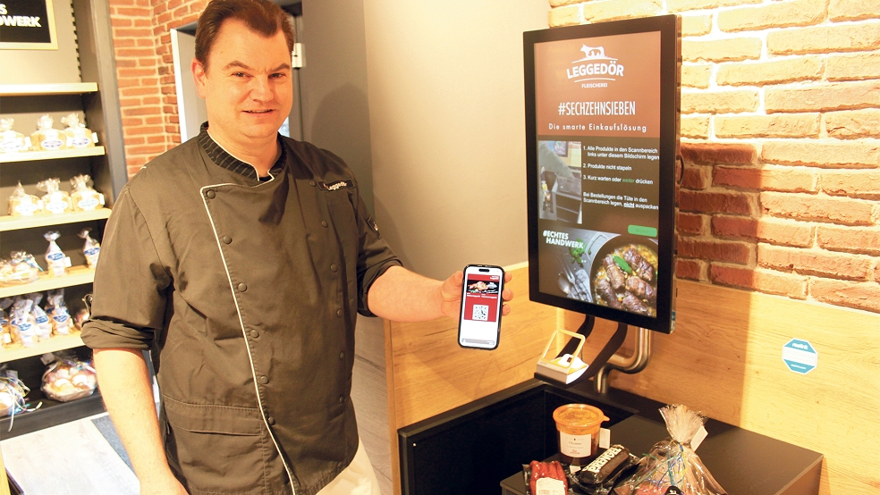 Inhaber Markus Leggedör hat einen QR-Code auf seinem Handy, mit dem er den Einkauf am Kassenscanner bezahlt.  © Foto: Busemann