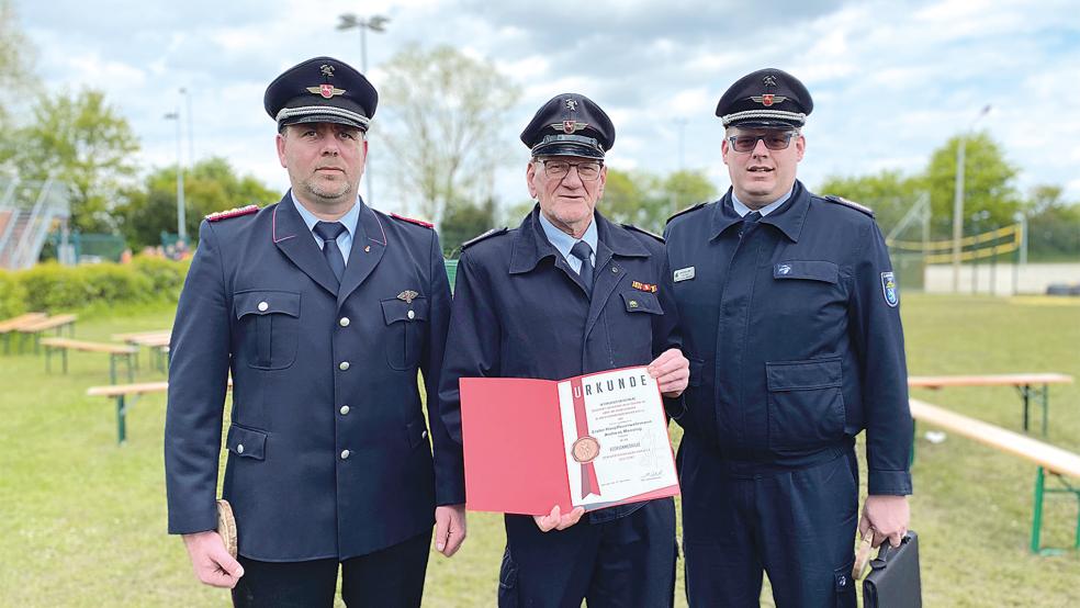 Jemgums Gemeindebrandmeister Jan Remmers (links) und Kreisjugendfeuerwehrwart Timo Smit (rechts) überreichten Andreas Mensing die Ukrunde..  © Foto: Kuper