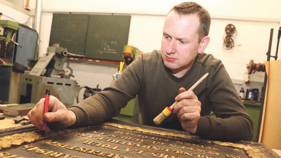 Zu neuem Glanz verhelfen: Keno Claassen reinigt die Gedenktafel vorsichtig von Farbresten und Dreck. Im Anschluss wird das Stück mit einem mikrokristallinen Wachs konserviert.  © Foto: Handwerkskammer