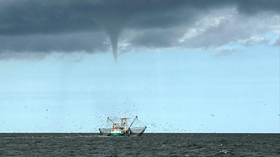 Das von einem Fischerboot aufgenommene Foto zeigt einen entstehenden mutmaßlichen Tornado vor der Nordseeinsel Borkum und ein Fischerboot. © Rolf Groenewold/dpa
