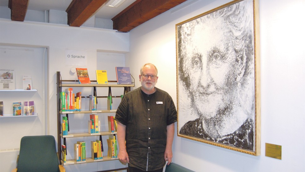 Bernhard Boekenkamp, Leiter der Stadtbibliothek Leer, vor einem Portrait der bekannten Leeraner Autorin Wilhelmine Siefkes. Die Regal-Lücken hinter ihm sollen gefüllt werden.  © Foto: Hoegen