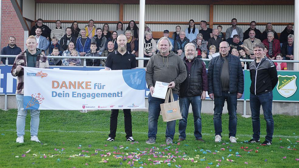 Dennis Siemons (vorne, mit Urkunde in der Hand) wurde vor der Tribüne, die er maßgeblich mitsaniert hat, mit einer Ehrung überrascht. Egge Mansholt (vorne, Dritter von rechts) vom Kreissportbund nahm die Ehrung vor.  © Foto: Born