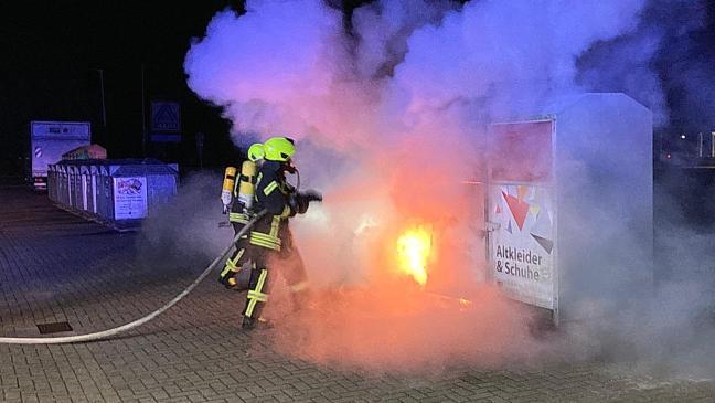 Drei Altkleidercontainer stehen in Flammen