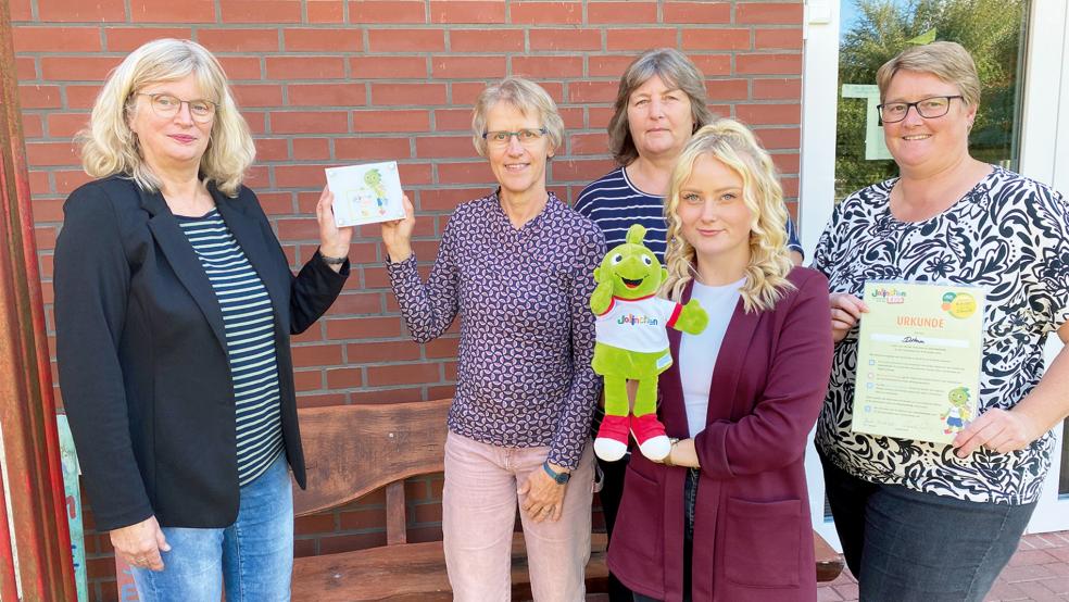 Die »Jolinchen«-Plakette der AOK soll neben dem Eingang des Kindergartens in Ditzum angebracht werden. Unser Bild zeigt die Übergabe mit (im Bild von links) Einrichtungsleiterin Renate Erchinger, AOK-Präventionsberaterin Marike Evers, Heidi Bugiel vom Freundeskreis Kindergarten Niederrheiderland, Sozialassistentin Leonie Bültjer und Kinderpflegerin Marion Raske.  © Foto: Kuper