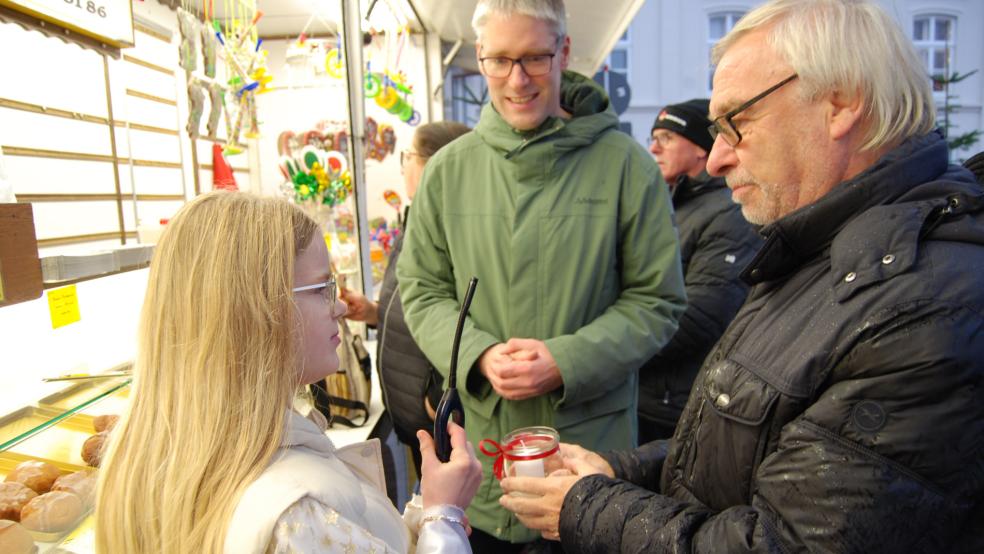 Weihnachtsengel Berit zündet eine Kerze am Berliner-Verkaufsstand von Würdemann an. Evert Pastoor als Vorsitzender der Werbegemeinschaft assistiert ihr dabei. In der Bildmitte Bürgermeister Heiko Abbas. © Hoegen